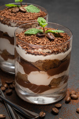two portions Classic tiramisu dessert in a glass on dark concrete background