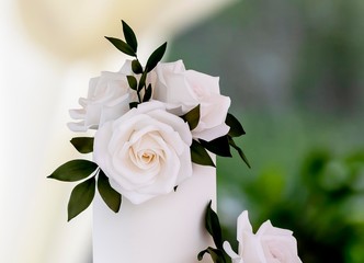 Close up of elegant minimalist wedding cake decorated with white roses on a table in a traditional summer marquee