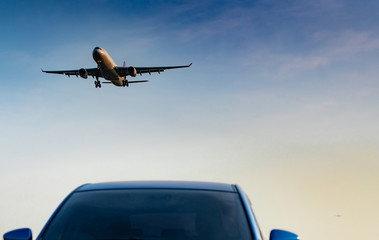 Fototapeta na wymiar Commercial airline. Passenger plane landing approach blue SUV car at airport with blue sky and clouds at sunset. Arrival flight. Vacation time. Happy trip. Airplane flying on bright sky. Car parked.