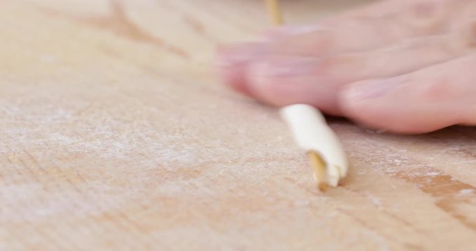 Mani di un uomo stanno impastando la pasta fatta in casa con farina, acqua e sale su un tagliere di legno in cucina.