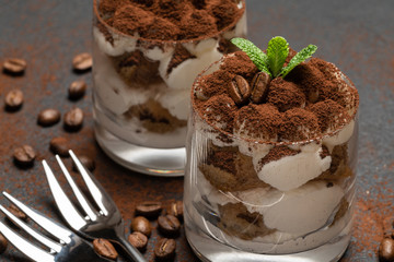 two portions Classic tiramisu dessert in a glass on dark concrete background