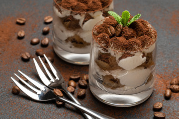 two portions Classic tiramisu dessert in a glass on dark concrete background