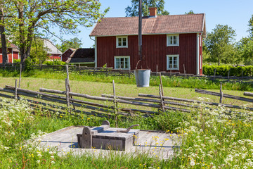 Old Water well in a meadow with a red old  cottage