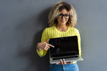 Smiling casual woman showing laptop screen over gray background. Looking at camera.