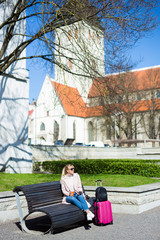 Obraz premium summer travel and vacation concept - young woman sitting with suitcase in old town of Tallinn, Estonia