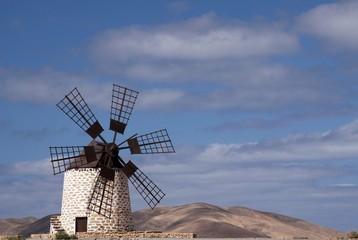 Isolated traditional windmill (Molino de Tefia) near La Olivia in dry arid hilly landscape against blue sky with cumulus clouds, Fuerteventura, Canary Islands
