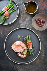 Barbecue marinated Greek lamb roast with kalamata olives and beans rolled in bacon as top view on a modern design plate