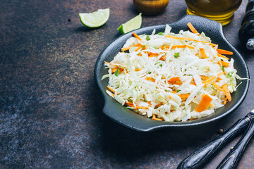 Fresh coleslaw salad in black plate on dark background.