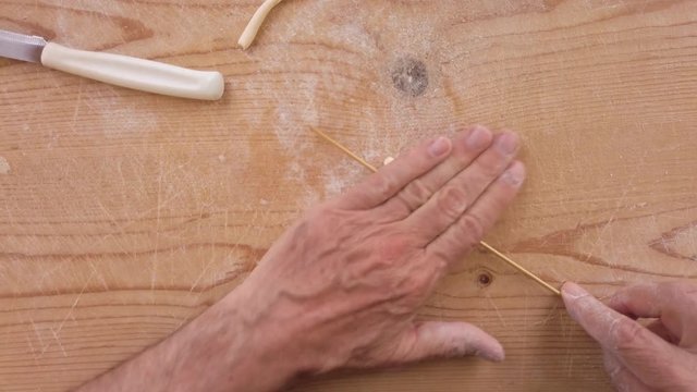 Mani di uno chef stanno preparando la pasta fatta in casa su un tagliere di legno con farina di semola e integrale.