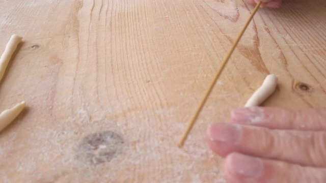 Mani di uno chef stanno preparando la pasta fatta in casa su un tagliere di legno con farina di semola e integrale.
