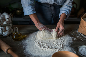 An experienced woman in a home kitchen prepares the dough with flour to make the Italian pasta. The concept of homemade healhty food. Italy, food, diet and bio food. Toned image. Selective focus.