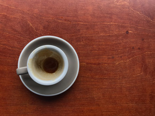 light gray cup and saucer of finished espresso coffee with stained brown coffee in a cup on brown wooden table with copy space on right side of frame