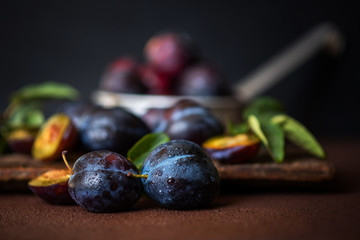 Plums in drops on dark wooden background. Half and whole of blue plum fruit. Many beautiful plums with leaves. Toned image. Selective focus.