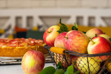 Ripe organic apples in vintage basket on rustic white table. Apple cheesecake in the background. Summer homemade apple tart with ingredients. Healthy organic food. Tasty breakfast.