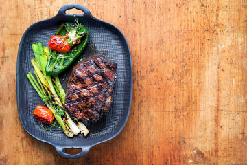 Barbecue dry aged wagyu entrecote beef steak with vegetable and herbs as top view on a gray cast iron pan with copy space right