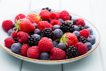 Fresh berry salad on blue dishes. Vintage wooden background.