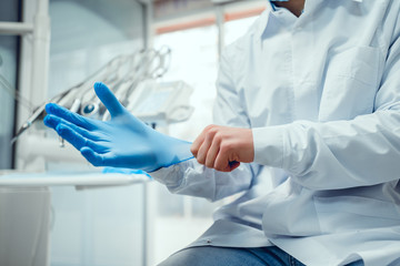 Close up view of male doctor's hands putting on blue sterilized surgical gloves in the medical...