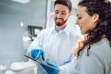 People, medicine, stomatology and health care concept - happy male dentist showing tablet pc computer to woman patient at dental clinic office.
