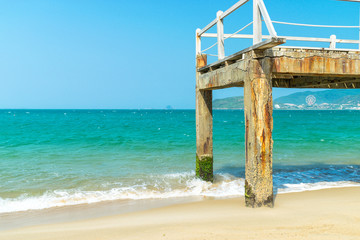 Old pier with moss over ocean with waves on beach in sunlight
