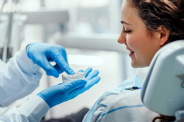 Male dentist showing his female patient how to brush teeth correctly, using dental mold. Mature...