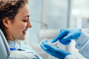 Male dentist explaining his female patient about teeth care, showing her dental mold. Professional...