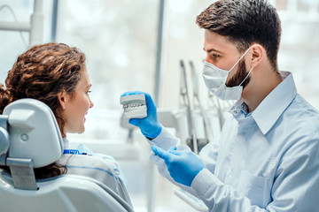 Dentist talking to his patient showing her dental mold. Side view.
