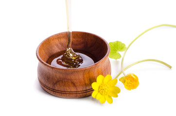 pouring honey in the wooden bowl with yellow flowers isolated on white background