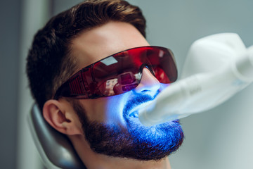 Teeth whitening. Man having teeth whitened by dental UV laser whitening device. Teeth whitening...