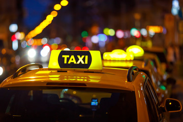 Yellow taxi cab and blurred city lights background at night with colorful bokeh - obrazy, fototapety, plakaty
