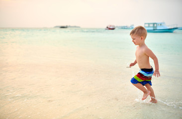 Three year old toddler boy on beach at sunset