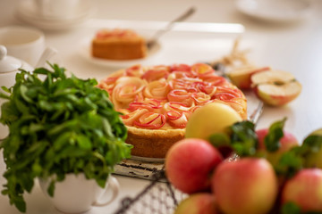 Ripe organic apples in vintage basket on rustic white table. Apple cheesecake in the background. Summer homemade apple tart with ingredients. Healthy organic food. Tasty breakfast.