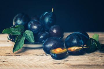 Garden plums on table. Close up of fresh plums with leaves. Summer or autumn harvest of plums. Toned image. Selective focus.