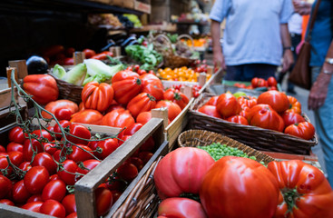 Farmers' food market stall with variety of organic vegetable. Vendor serving and chating with customers.