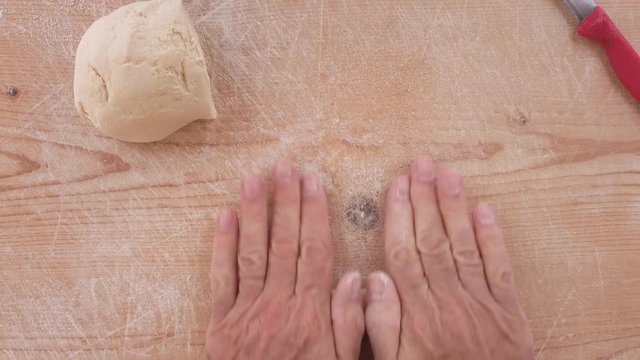 Mani di uno chef stanno preparando la pasta fatta in casa su un tagliere di legno con farina di semola e integrale.