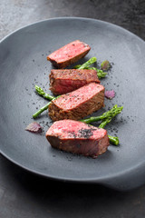 Barbecue dry aged wagyu fillet steak with blanched green asparagus tips and herbs as closeup on a modern design plate with copy space