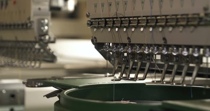 In slow motion video in a garment factory, a sewing machine embroiders various companies and engravings. Concept of: Automated work, Sewing machine, Engraving, Thread, Fabric, Needle.