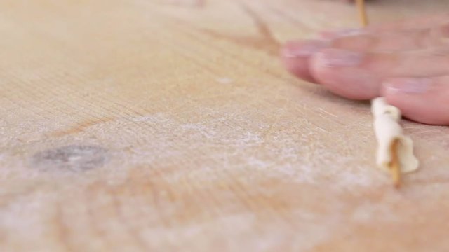 Mani di uno chef stanno preparando la pasta fatta in casa su un tagliere di legno con farina di semola e integrale.