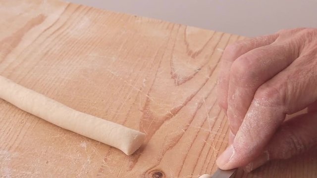 Mani di uno chef stanno preparando la pasta fatta in casa su un tagliere di legno con farina di semola e integrale.