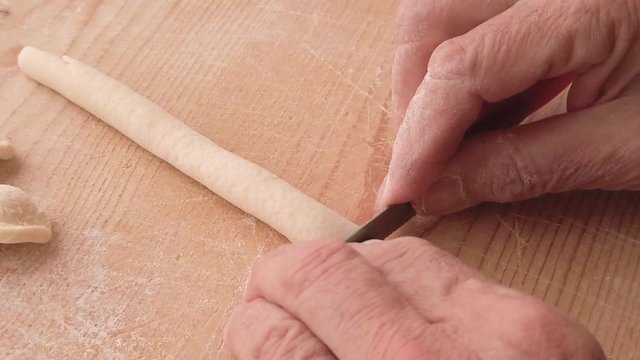 Mani di un uomo stanno impastando la pasta fatta in casa con farina, acqua e sale su un tagliere di legno in cucina.