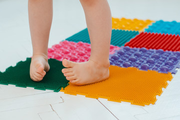 Toddler on baby foot massage mat. Exercises for legs on orthopedic massage carpet. prevention of flat feet and hallux valgus