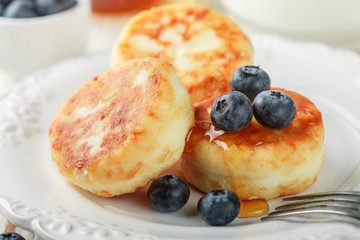 Cottage cheese pancakes, syrniki, curd fritters with fresh berries blueberry and honey in a white plate. Gourmet Breakfast. Selective focus