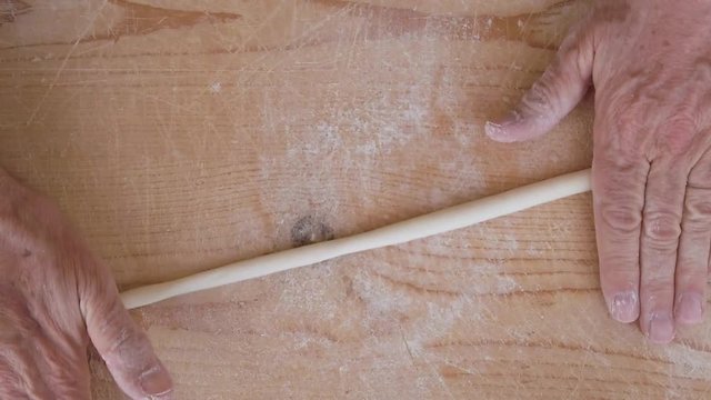 Mani di uno chef stanno preparando la pasta fatta in casa su un tagliere di legno con farina di semola e integrale.