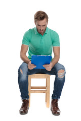 seated surprised guy in green polo shirt looking at notepad