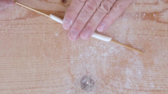 Mani di un uomo stanno stendendo la pasta filata fatta in casa su un tagliere di legno.