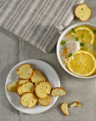 Delicious chicken soup with lemon, rise, carrot, green onion and yellow bruschette chips. Top view. Rustic tablecloth. Striped serviette. Space for a text. Nice layout. Food background.