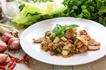 Close up Popular Thai cuisine, spicy sliced grilled pork salad recipe for Larb Nam Tok  with mint leaves on top on wooden table background . Traditional food of Thailand .  Thai north eastern foods.