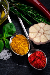 Various Spices in metal spoon. Curry, turmeric, rosemary, garlic, paprika, pepper, salt, basil, thyme on dark wooden background. Mix of Indian herbal cuisine