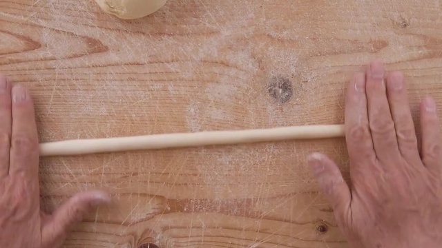 Mani di uno chef stanno preparando la pasta fatta in casa su un tagliere di legno con farina di semola e integrale.