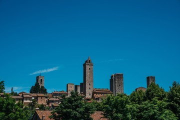 San Gimignano town skyline and medieval towers on tne sky background. Trees in foreground. Tuscany, Italy, Europe. Summer, holiday, traveling concept.