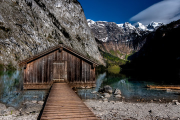 Fototapeta na wymiar very old, wooden fishing hut standing on the water in Obersee Königssee, located among the peaks of the Bavarian Alps